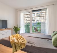 I Slnečnice – Zóna mesto moderný 1-izb byt s loggiou - Spálňa v 1-izbovom byte s televízorom, zrkadlami a balkónom, podlaha s dreveným dekorom.
