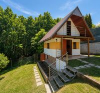 Záhrada s murovanou chatkou a výhľadom, Považská Bystrica -Klučina - Chata s dreveným dekorom v Považskej Bystrici na Klučine, obklopená zeleňou a stromami.