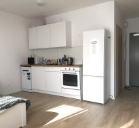 Prenájom 1 izb. byt, NOVOSTAVBA Ivanská cesta, Bratislava II, Trnávka  - Kuchynská časť v 1-izbovom byte s podlahou s dreveným dekorom a bielym nábytkom.