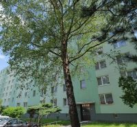 Na predaj - 3i BYT s veľkorysou výmerou - centrum PB - Považská Bystrica, Štúrova: Panelový dom obklopený stromami a zaparkovanými autami na ulici.