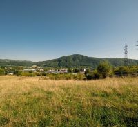 Na predaj stavebný pozemok pre rodinné domy – Banská Bystrica P306ZL - Krajina s trávnatým pozemkom a elektrickými stĺpmi na Partizánskej ceste, Banská Bystrica. Pozemky - bývanie.