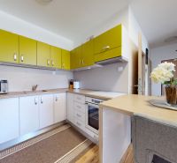 Moderný 3-izbový byt s balkónom a 2 parkovacími miestami - Ludanice - Kuchyňa s bielymi a žltými skrinkami, mikrovlnkou a dekoratívnymi kvetmi v 3-izbovom byte.
