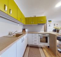 Moderný 3-izbový byt s balkónom a 2 parkovacími miestami - Ludanice - Kuchyňa s farebnými skrinkami a podlahou s dreveným dekorom v 3-izbovom byte.