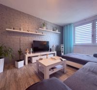 Na predaj: 4 izb.byt + BALKON + PIVNICA - Obývacia izba v 4-izbovom byte s podlahou s dreveným dekorom a sivými závesmi.