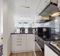 | Zariadený 1,5 izbový byt | 35m² | SLNEČNICE - Kuchyňa v 2-izbovom byte s lesklou pracovnou doskou a zrkadlom na stene.