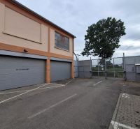 Na prenájom skladové priestory od 25 m2 Trnava Coburgova - Exteriér skladu a hál na Coburgovej ulici v Trnave, s veľkými bránami a stromom.