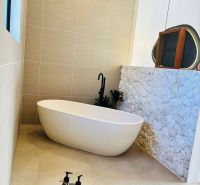 VILA AURA – FREE HOLD VLASTNÍCTVO S PRIAMYM VÝHĽADOM NA SOPKU AGUNG - Kúpeľňa v rodinnom dome s voľne stojacou vaňou a kamenným obkladom steny.