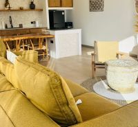 VILA AURA – FREE HOLD VLASTNÍCTVO S PRIAMYM VÝHĽADOM NA SOPKU AGUNG - Interiér rodinného domu s pohovkou, kuchyňou, ratanovými stoličkami a doplnkami z prírodných materiálov.