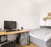 Predaj príjemný 2 izbový byt, Rovníková ulica, Bratislava II. Ružinov - Spálňa v 2-izbovom byte s posteľou, stolom a podlahou s dreveným dekorom.