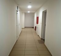 Priestranná garzónka s balkónom v novostavbe. - Chodba s bielymi stenami, dlažbou a núdzovým vybavením v Garsónke.