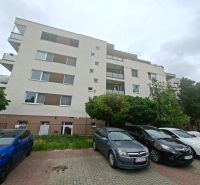 Priestranná garzónka s balkónom v novostavbe. - Bytový dom na Športovej ulici v Dunajskej Lužnej s parkoviskom a autami pred budovou.
