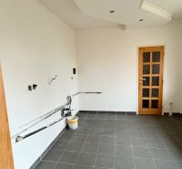 Slnečný 2-izbový byt vo vynikajúcej lokalite – stačí dokončiť kuchyňu  - Prázdna miestnosť v 2-izbovom byte, podlaha z tmavej dlažby, biele steny, drevené dvere.