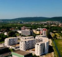 PREDAJ ELEGANTNÝ 2-IZBOVÝ BYT S BALKÓNOM A PARKOVANÍM V RAČI - Pohľad na obytné budovy a okolitú zeleň v Bratislave III, vhodné pre 2-izbový byt.