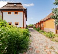 PREDAJ RODINNÝ DOM+OBJEKTY+POZEMOK S INVESTIČNÝM POTENCIÁLOM - Rodinný dom v Nových Zámkoch s oranžovou fasádou a upravenou dlažbou v záhrade.