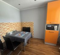 3 izbový byt 75m2, ul.Bruselská, Košice- Ťahanovce - Kuchyňa s oranžovou kuchynskou linkou, jedálenským stolom a podlahou s dreveným dekorom.