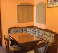 Prenájom 2 izbový byt Poprad - loggia - Kuchynský kút so sedačkou v 2-izbovom byte, podlaha s dreveným dekorom, oranžové steny.