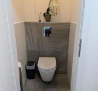 Moderný 2-izbový byt s balkónom a výhľadom - Toaleta v 2-izbovom byte s šedým obkladom a rastlinou na poličke.