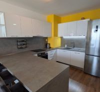 Moderný 2-izbový byt s balkónom a výhľadom - Kuchyňa v 2-izbovom byte s bielymi skrinkami, žltou stenou a podlahou s dreveným dekorom.