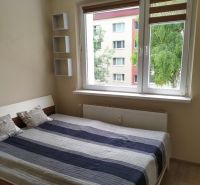 TOP PONUKA: Kompletne zrekonštruovaný a zariadený 2-izbový byt - Spálňa s veľkým oknom, posteľou, nástennými poličkami a podlahou s dreveným dekorom.