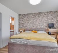 4-izbový rodinný dom v lukratívnej časti Trnavy Kamenáč - Spálňa s kamenným efektom steny, podlaha s dreveným dekorom, postel a pracovný kútik.