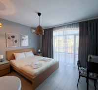 Moderná garsónka (41 m²) s výhľadom na bazén – Rezort ANTARES - Garsónka s podlahou v dekore dreva, veľkou posteľou a závesmi na okne.