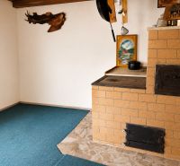 Menší Rodinný dom Veľké Košecké Podhradie, pozemok 340 m2 - Kachľová pec v rohu rodinného domu s keramickou dlažbou a obrazom na stene.