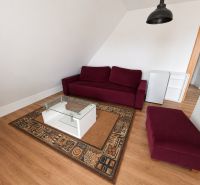 Prenájom, Apartmán v meste Krupina - Obývačka s červenou sedačkou, stolíkom na koberci a podlahou s dreveným dekorom.