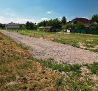 Projekt ČEREŠŇOVÁ ALEJ – 10 rod. domov/pozemk., Jelka - Pozemok pri rodinných domoch v Jelke s kamenistou cestou a zeleňou okolo.