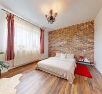 5 izbový rodinný dom v Malinove | 751 m² pozemok - Spálňa s tehlovou stenou, podlaha s dreveným dekorom, rastlina a luster.