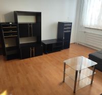 Na prenájom zariadený 3 izbový byt v Nových Zámkoch - Obývacia izba s čiernym nábytkom, skleneným stolíkom a podlahou s dreveným dekorom.