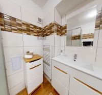  PRENÁJOM 2-izbový byt, centrum mesta s vlastným parkovaním, Topoľčany - Kúpeľňa v 2-izbovom byte s bielym nábytkom, zrkadlom a podlahou s dreveným dekorom.