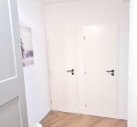 Prenájom 2 izb. bytu Račianske mýto, Bratislava - Biela chodba v 2-izbovom byte, podlaha s dreveným dekorom, umenie na stene.