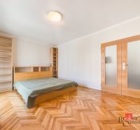 Staromestský 2i byt s balkónom na Palisádach - Spálňa v 2-izbovom byte s posteľou, knihovňami a podlahou s dreveným dekorom.