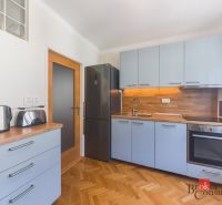 Staromestský 2i byt s balkónom na Palisádach - Kuchyňa v 2-izbovom byte s podlahou s dreveným dekorom a bielymi skrinkami.