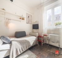 Praktická garsónka v Starom meste - Garsónka so svetlým interiérom, posteľou, poličkami a priehľadnou stoličkou, s dlažbou na podlahe.