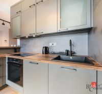Elegantný 2i byt s lodžiou a výhľadom na Dunaj vo Vydrici - Kuchyňa v 2-izbovom byte s podlahou s dreveným dekorom, s moderným vybavením a skrinkami.