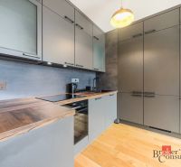 Elegantný 2i byt s lodžiou a výhľadom na Dunaj vo Vydrici - Kuchyňa v 2-izbovom byte s podlahou s dreveným dekorom a sivými skrinkami.
