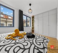Moderný 2i apartmán v novostavbe v Starom Meste - Spálňa v 2-izbovom byte s veľkými oknami, vstavanou skriňou a podlahou s dreveným dekorom.