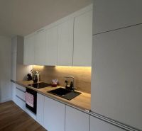 Moderný 2i apartmán v novostavbe v Starom Meste - Kuchyňa v 2-izbovom byte s bielymi skrinkami a podlahou s dreveným dekorom.