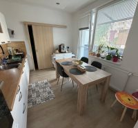 3 izbový byt s balkónom Topoľčany  - Kuchyňa v 3-izbovom byte s podlahou s dreveným dekorom a jedálenským stolom.