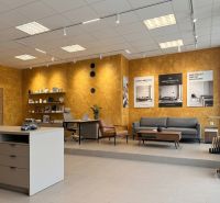 Prenájom 148,25 m² showroom, predajňa | Zlatovce - Interiér obchodných priestorov, sedenie, stôl, žlté steny, podlaha s dreveným dekorom.