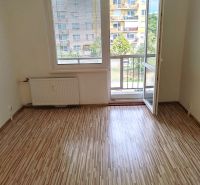 1 izbový byt s balkónom na prenájom  - Izba s podlahou s dreveným dekorom, balkónovými dverami a výhľadom na sídlisko.