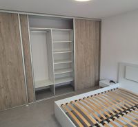 Na prenájom kompletne prerob. NOVÝ 2 izbový byt čiast.zar. Nové Zámky - Spálňa v 2-izbovom byte s posteľou a skriňou s dreveným dekorom.