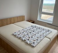 Kompletne zariadený 3-izbový byt s balkónom | PRÚDY Trnava - Spálňa v 3-izbovom byte s podlahou s dreveným dekorom a výhľadom z okna.