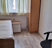 3- izbový byt na ulici Hany Meličkovej  - Izba s posteľou, stolíkom, skriňou a podlahou s dreveným dekorom v 3-izbovom byte.