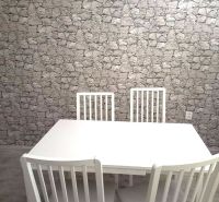 3- izbový byt na ulici Hany Meličkovej  - Biely jedálenský stôl so štyrmi stoličkami, kamenná tapeta, podlaha s dreveným dekorom.