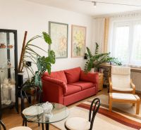 2- izbový byt na  ulici Studenohorská, Bratislava-Lamač - Obývacia izba 2-izbového bytu s červenou sedačkou a veľkými rastlinami.