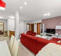  | 3 izbový byt o výmere 73m2 + balkón - Obývačka s červenou pohovkou, kuchyňou a podlahou s dreveným dekorom v 3-izbovom byte.