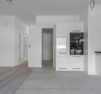 Na predaj nový moderný 4-izbový rodinný dom s terasou a záhradou - Interiér rodinného domu s bielou kuchynskou linkou a podlahou s dreveným dekorom.