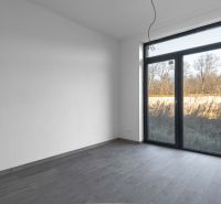 Na predaj nový moderný 4-izbový rodinný dom s terasou a záhradou - Izba v rodinnom dome s veľkým oknom a podlahou s dreveným dekorom.